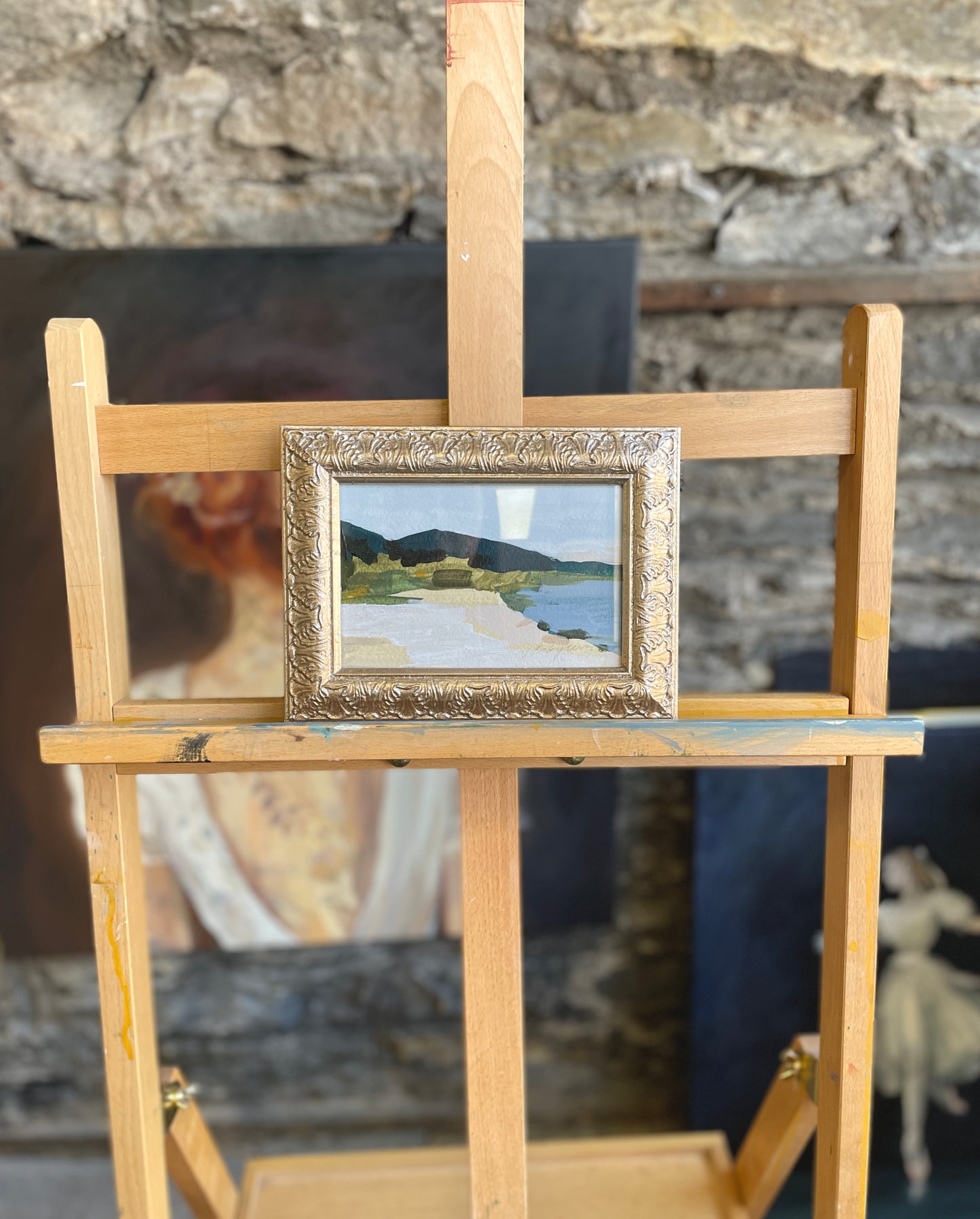 A small, framed artwork featuring an abstract landscape of a mountain and tranquil body of water.